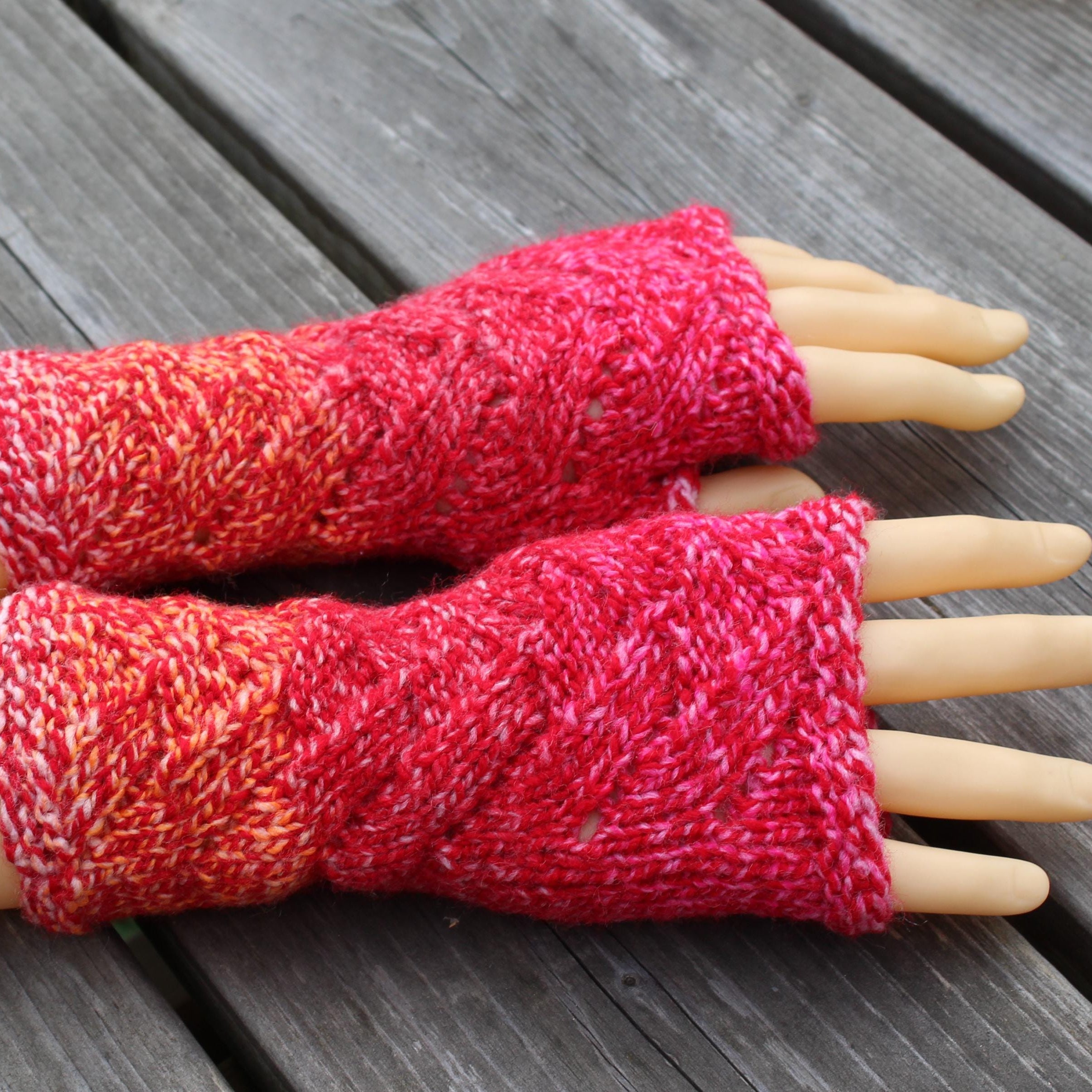 Red knitted fingerless gloves on a mannequin hand against a wooden background