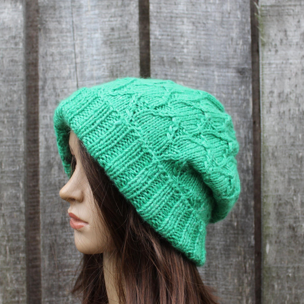 Green knitted beanie on a mannequin head against a wooden fence background