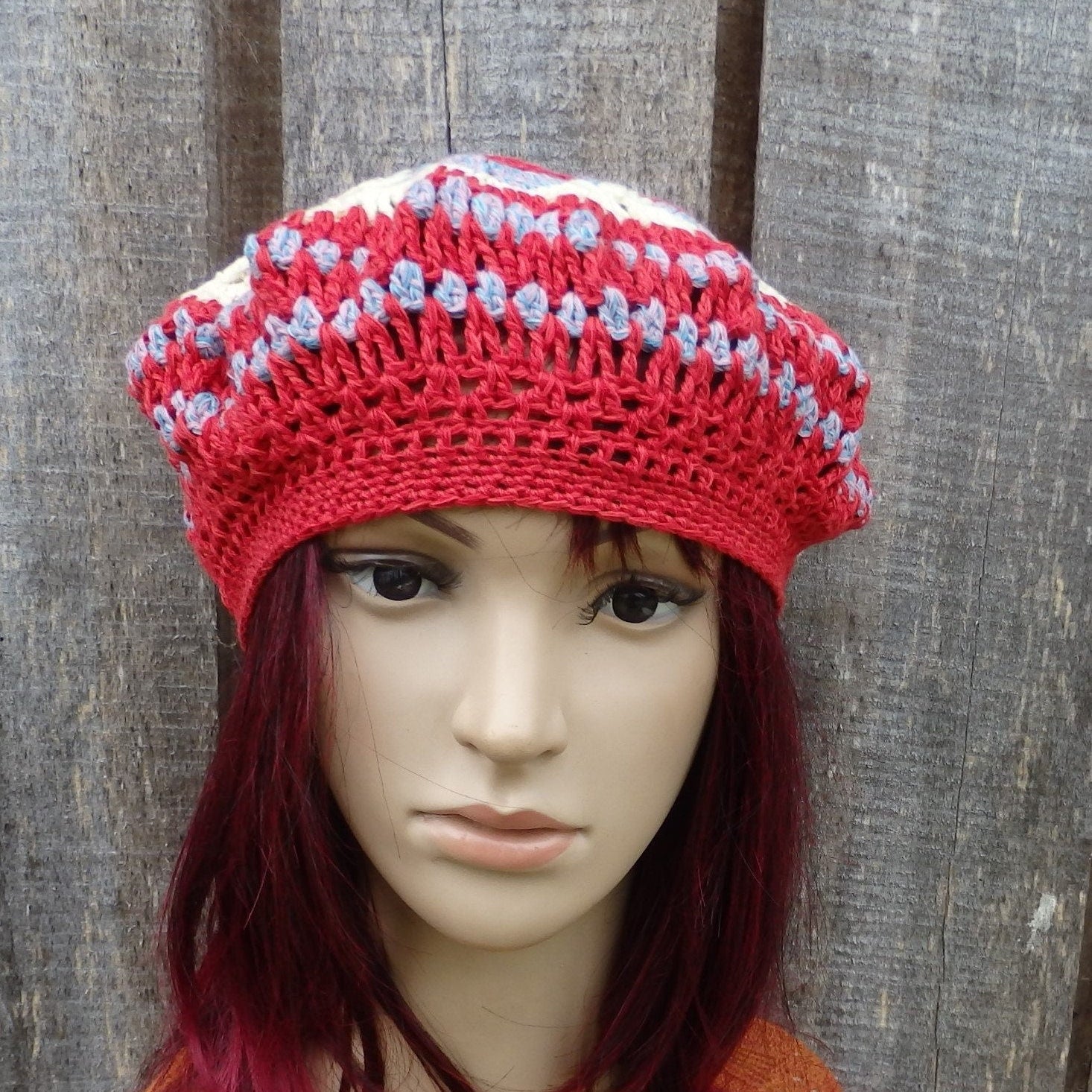 Red and white striped crochet hat on a mannequin head against a wooden background