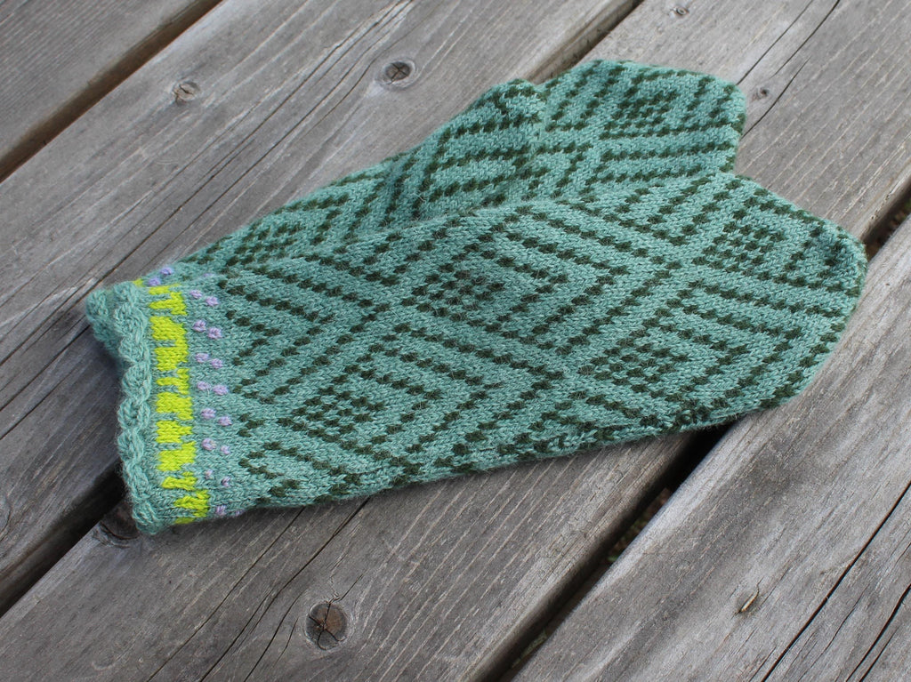 Green knitted mitten with a pattern on a wooden surface