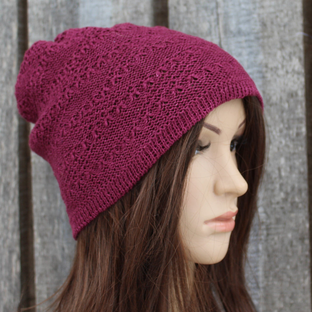 Maroon knitted beanie worn by a person against a wooden background