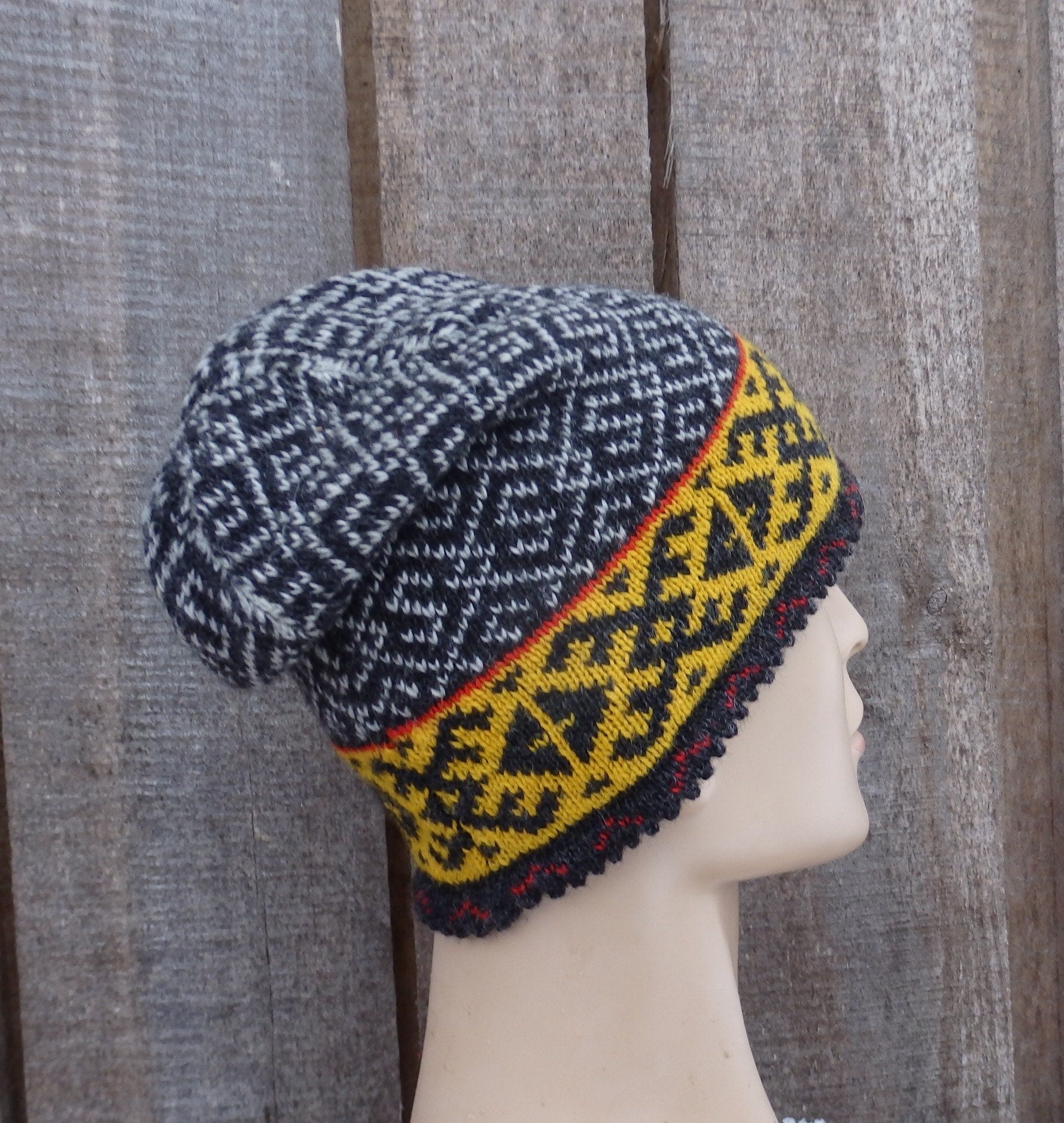Knitted hat with a patterned yellow and red trim on a mannequin head against a wooden background