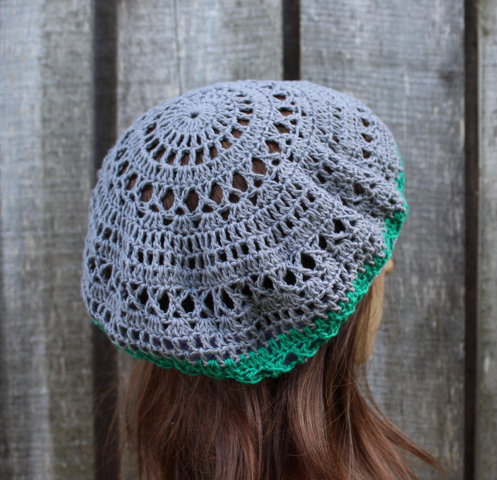 Gray and green crocheted beanie worn by a person against a wooden background