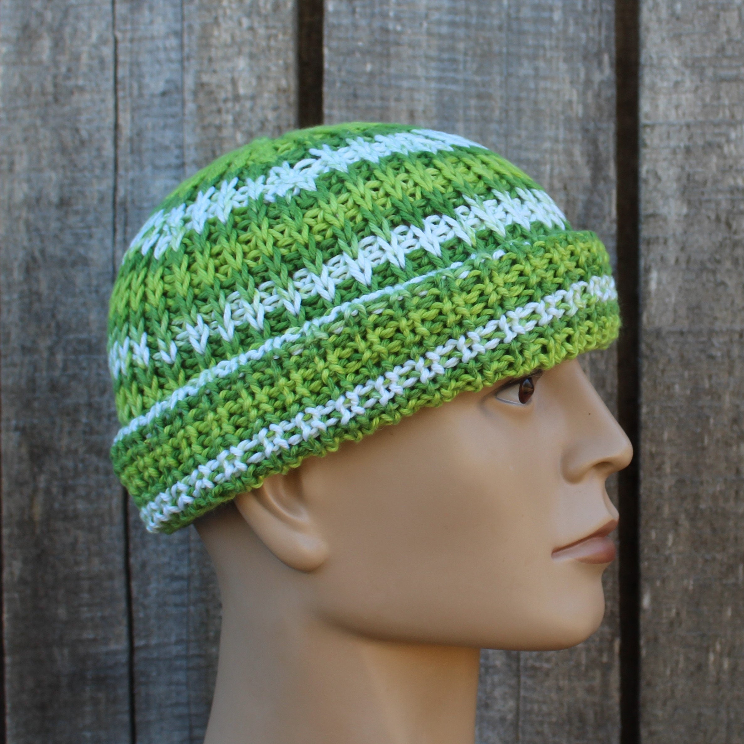 Green and white striped knitted beanie on a mannequin head against a wooden background