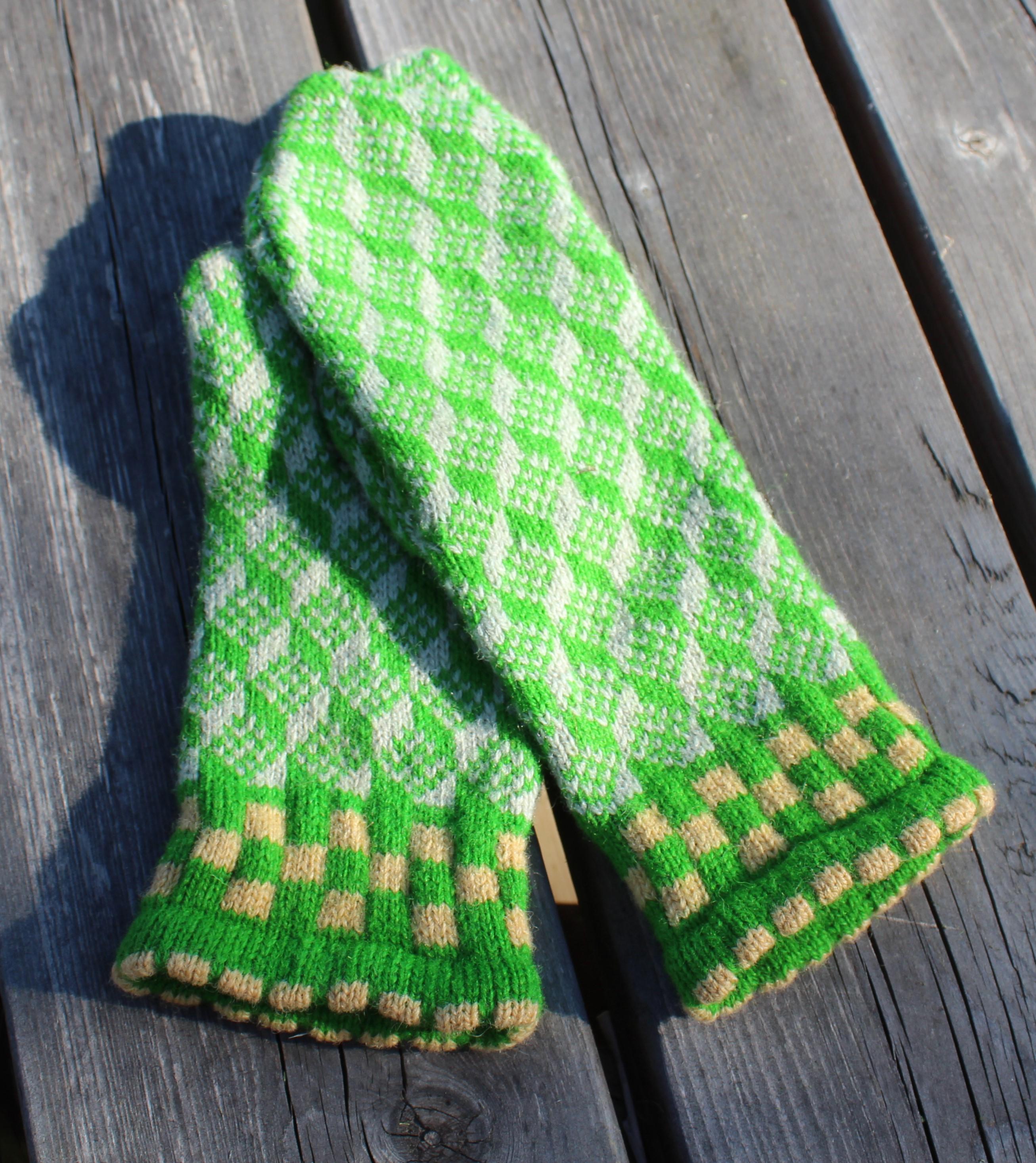 Green and white checkered mittens on a wooden surface