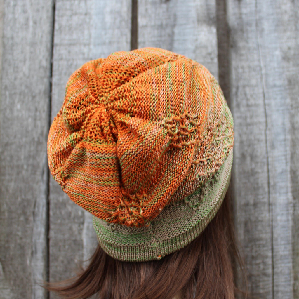Knitted hat with orange and green pattern against a wooden background