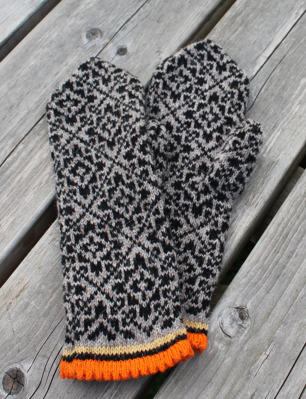 Pair of patterned mittens with orange cuffs on a wooden surface