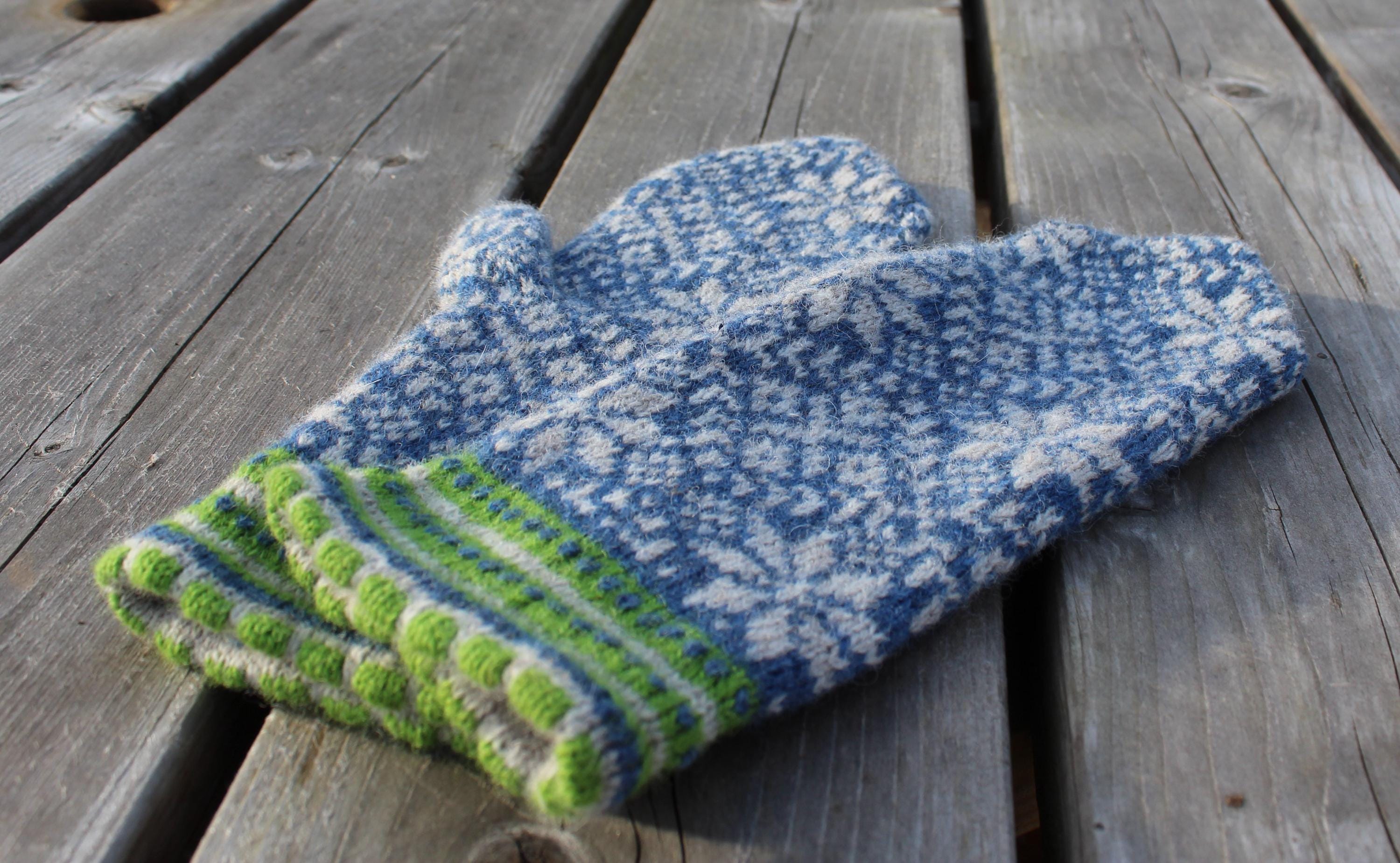 Pair of blue and green knitted mittens on a wooden surface