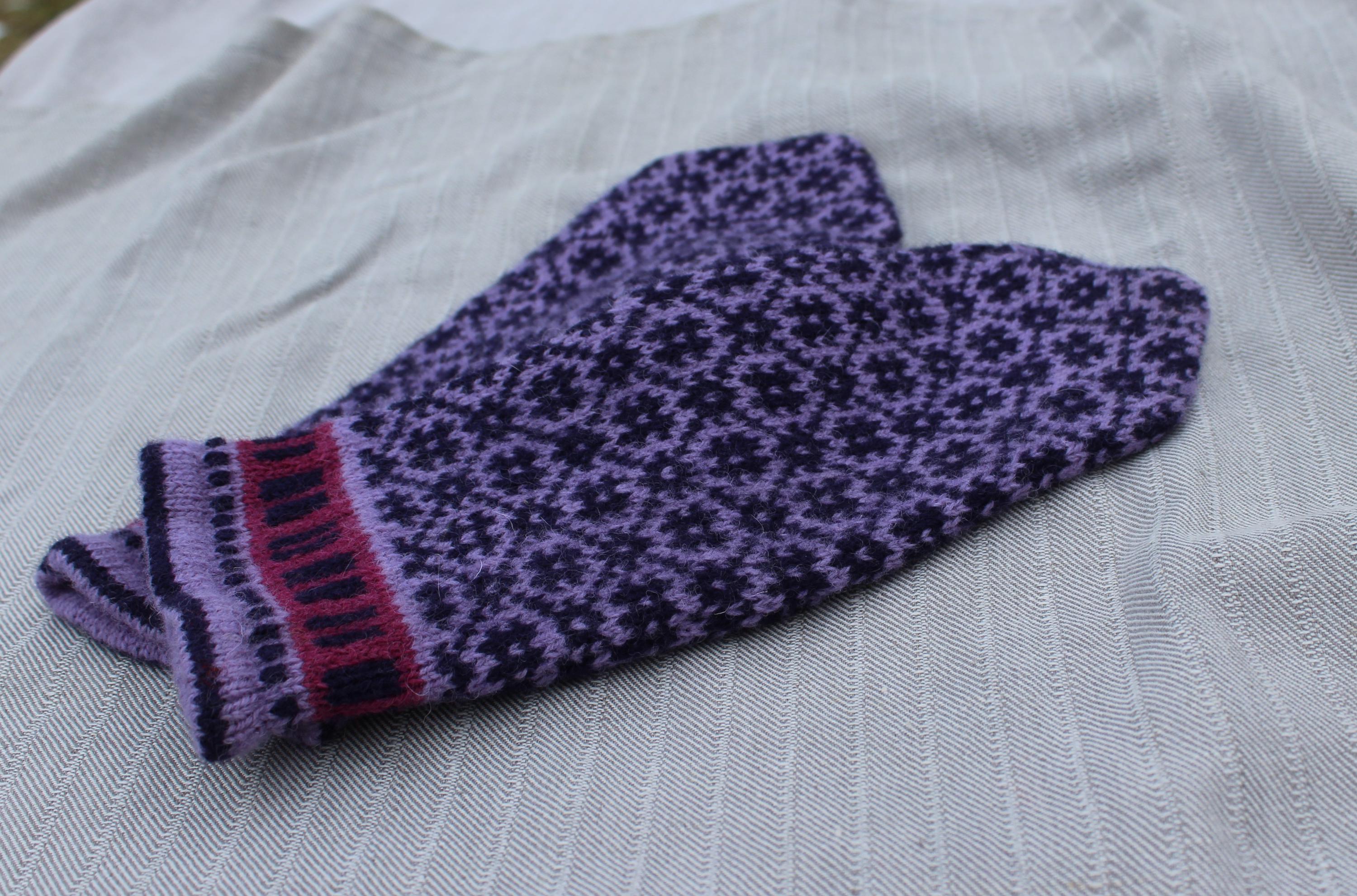 Purple knitted glove with black pattern on a white fabric background