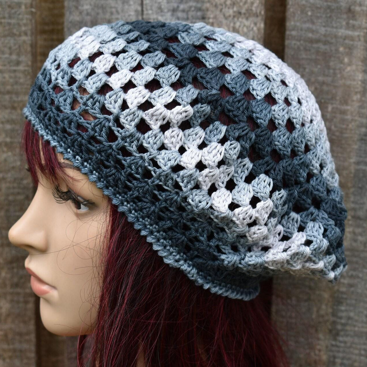 Person wearing a crocheted blue and gray hat against a wooden background