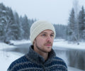 Man wearing a wool  hat and sweater in a snowy landscape with trees and water.