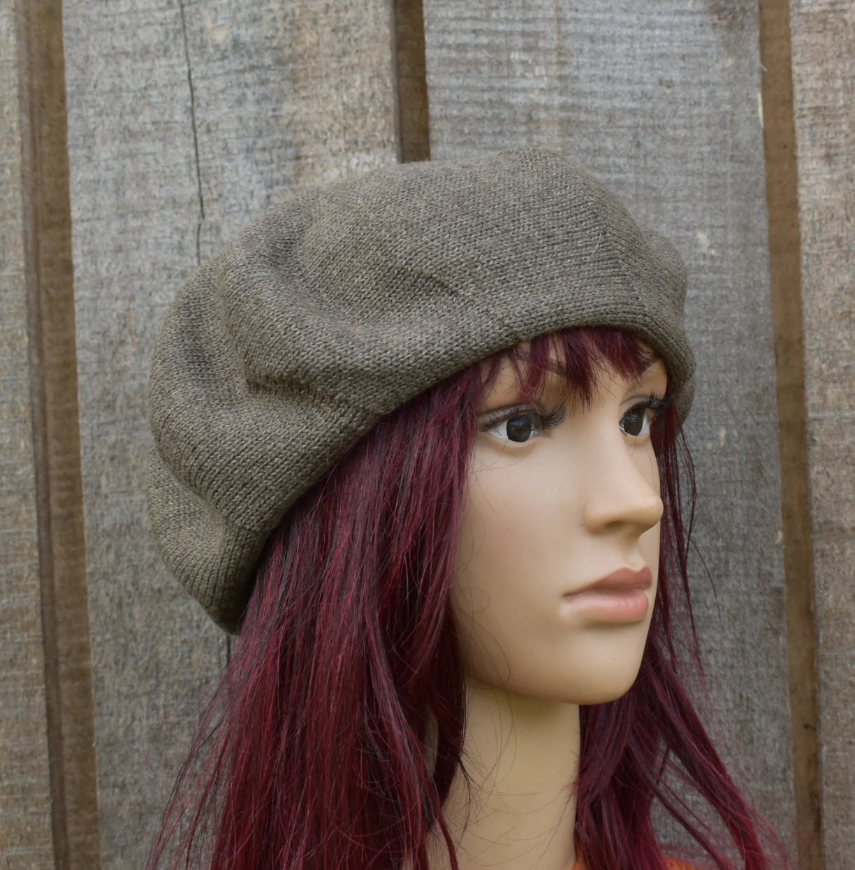 Mannequin head wearing a brown beret against a wooden panel background