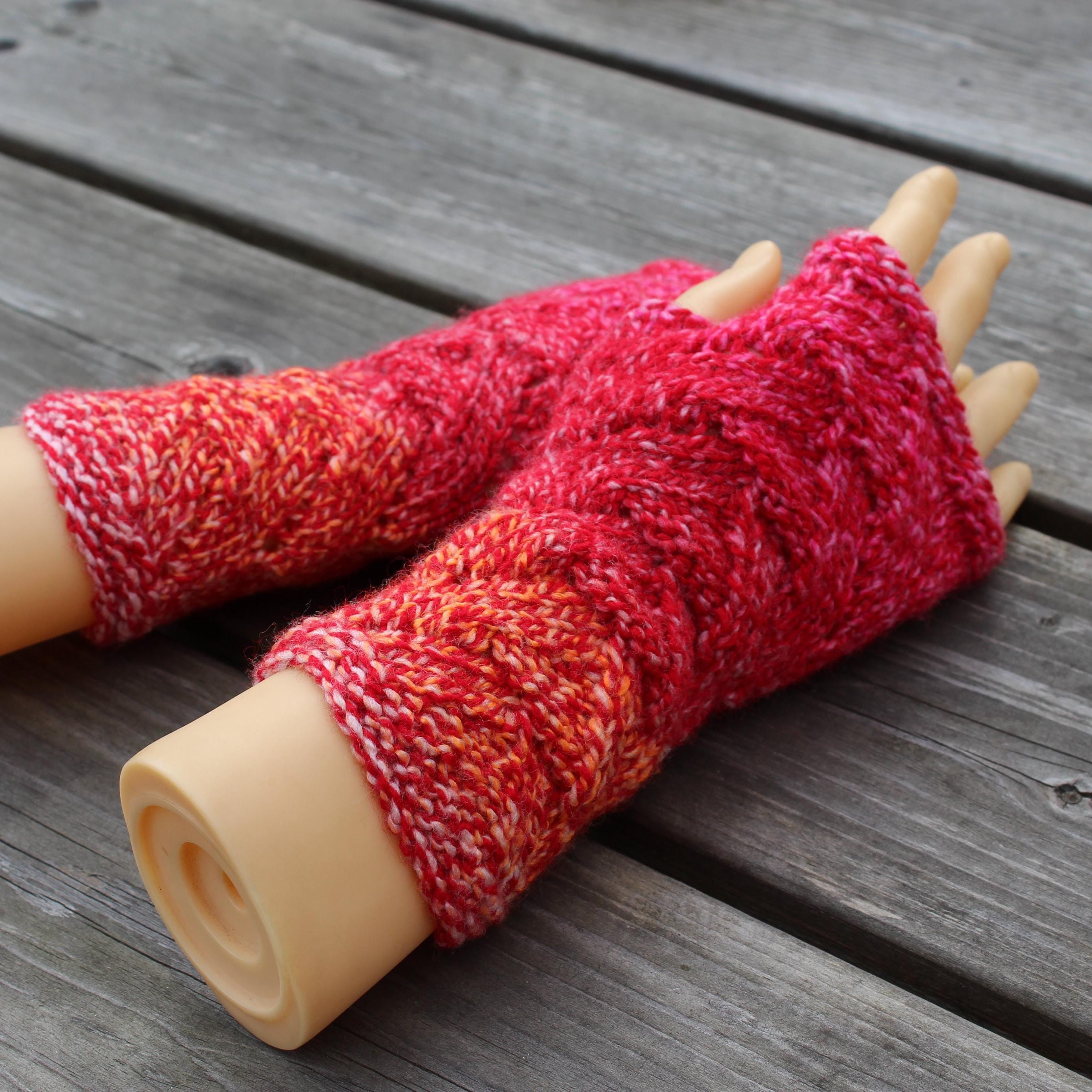 Red and orange knitted arm warmers on a wooden surface