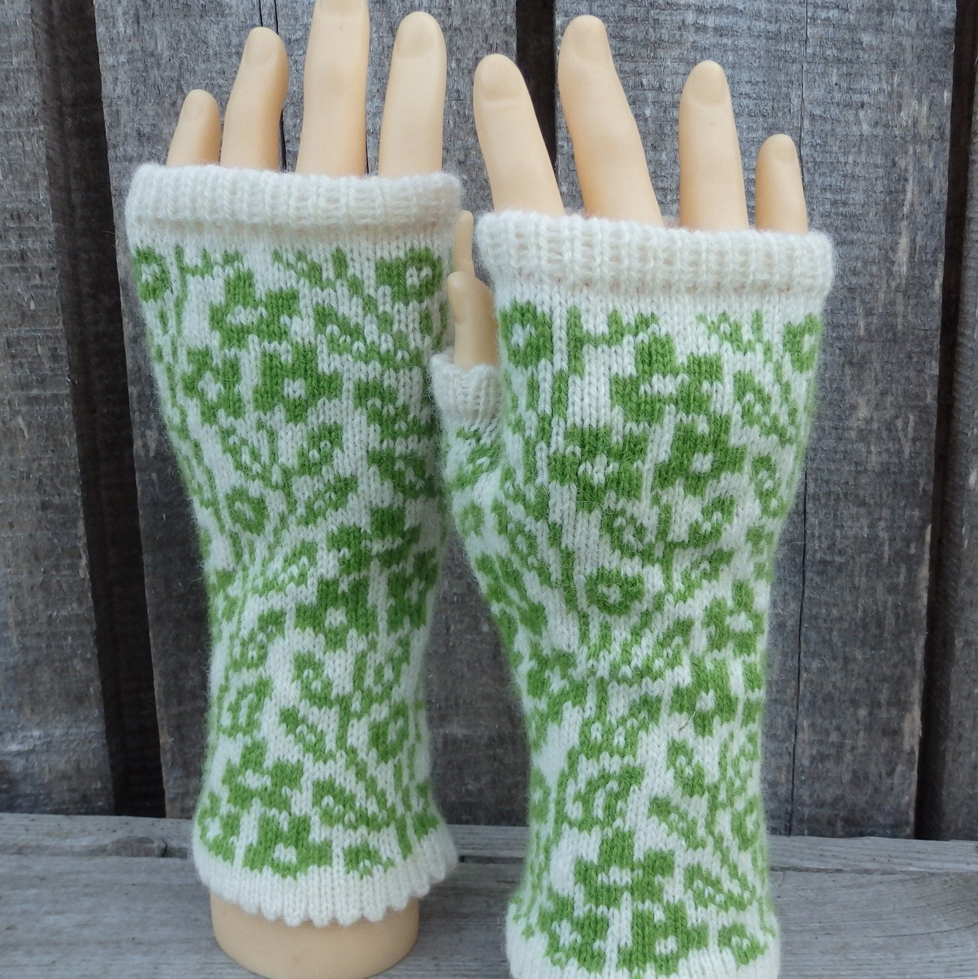 Green and white patterned fingerless gloves on a wooden mannequin hand against a wooden background