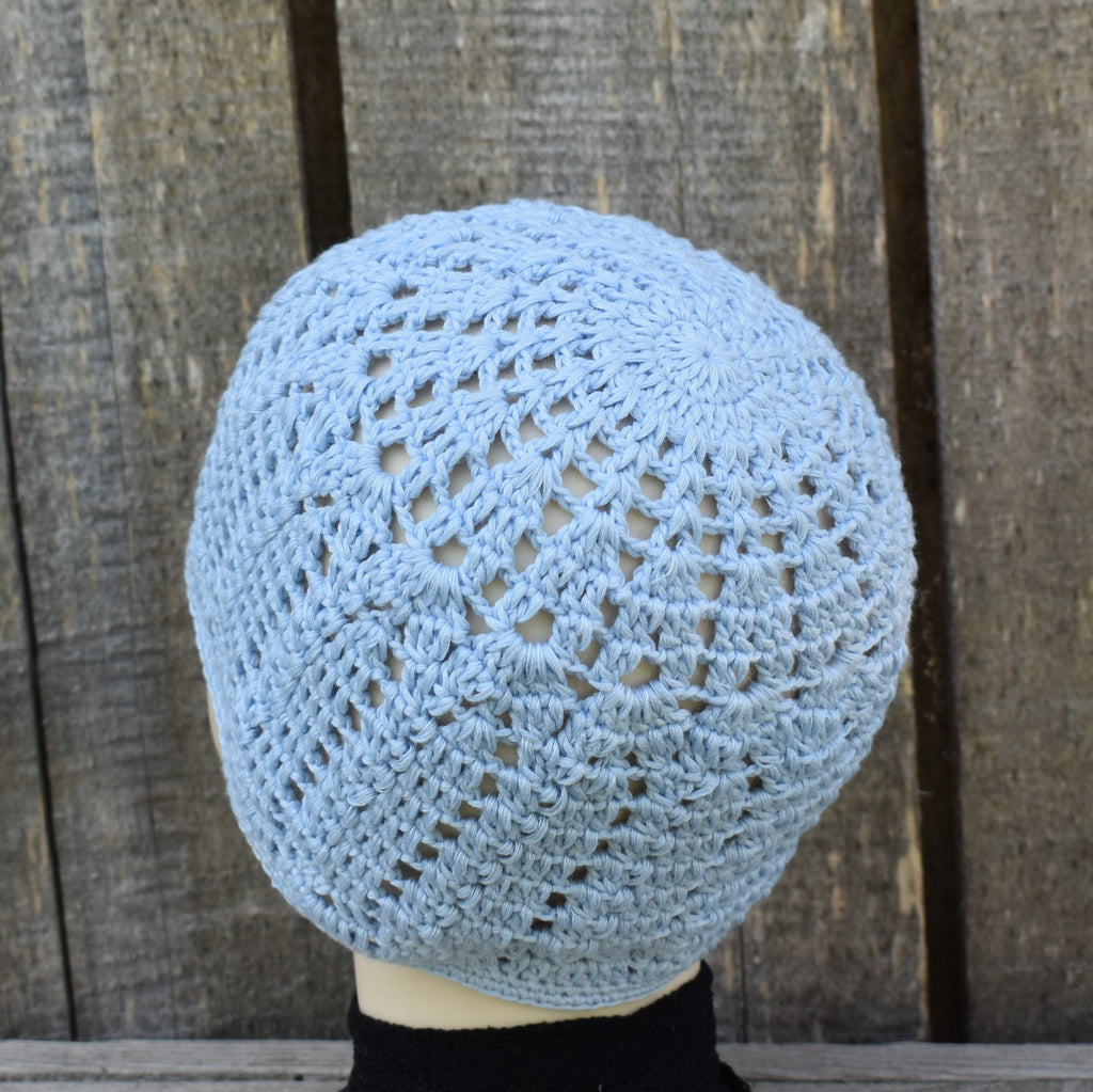 Light blue crocheted hat on a mannequin head against a wooden background