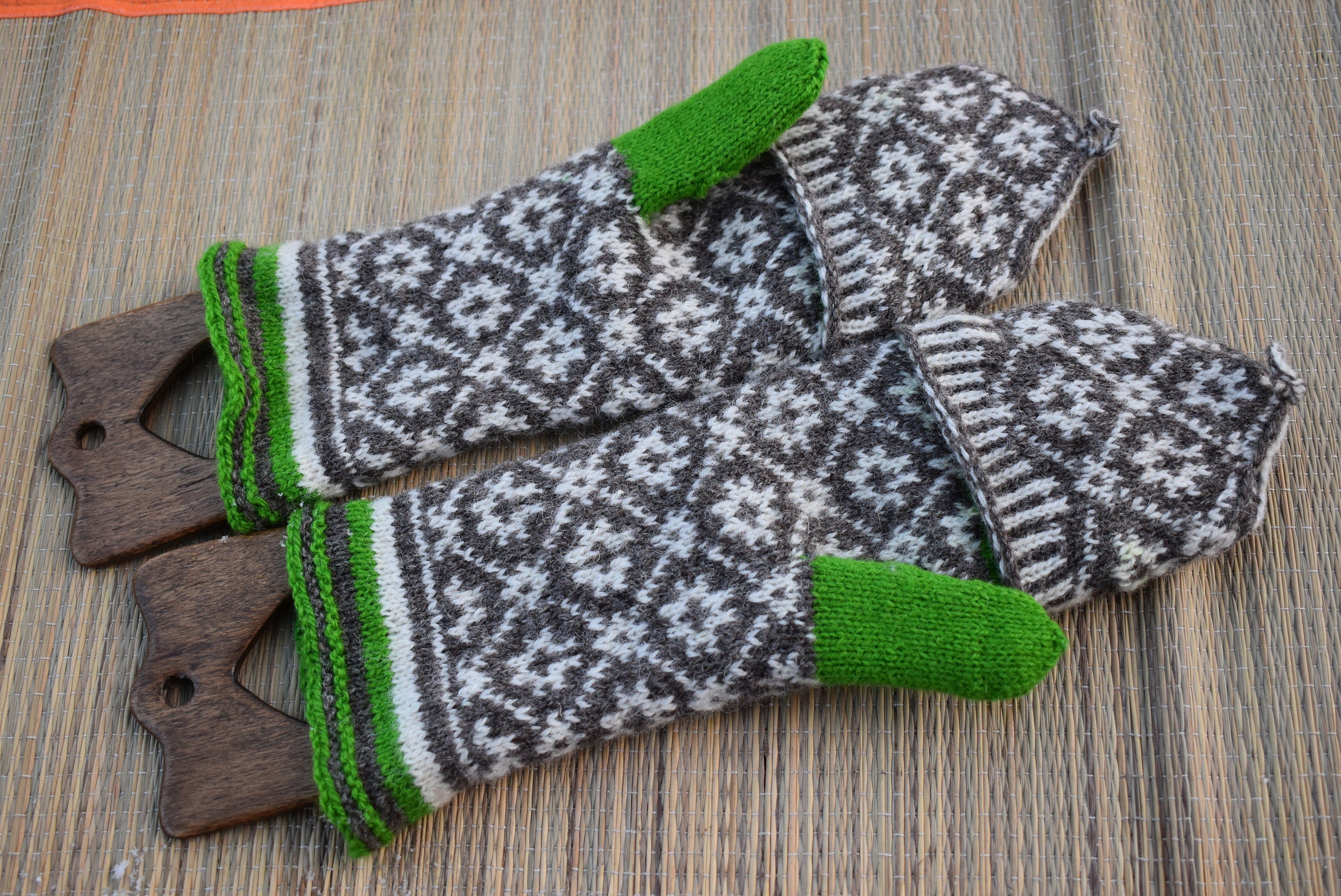 Pair of knitted mittens with green accents on a wooden surface