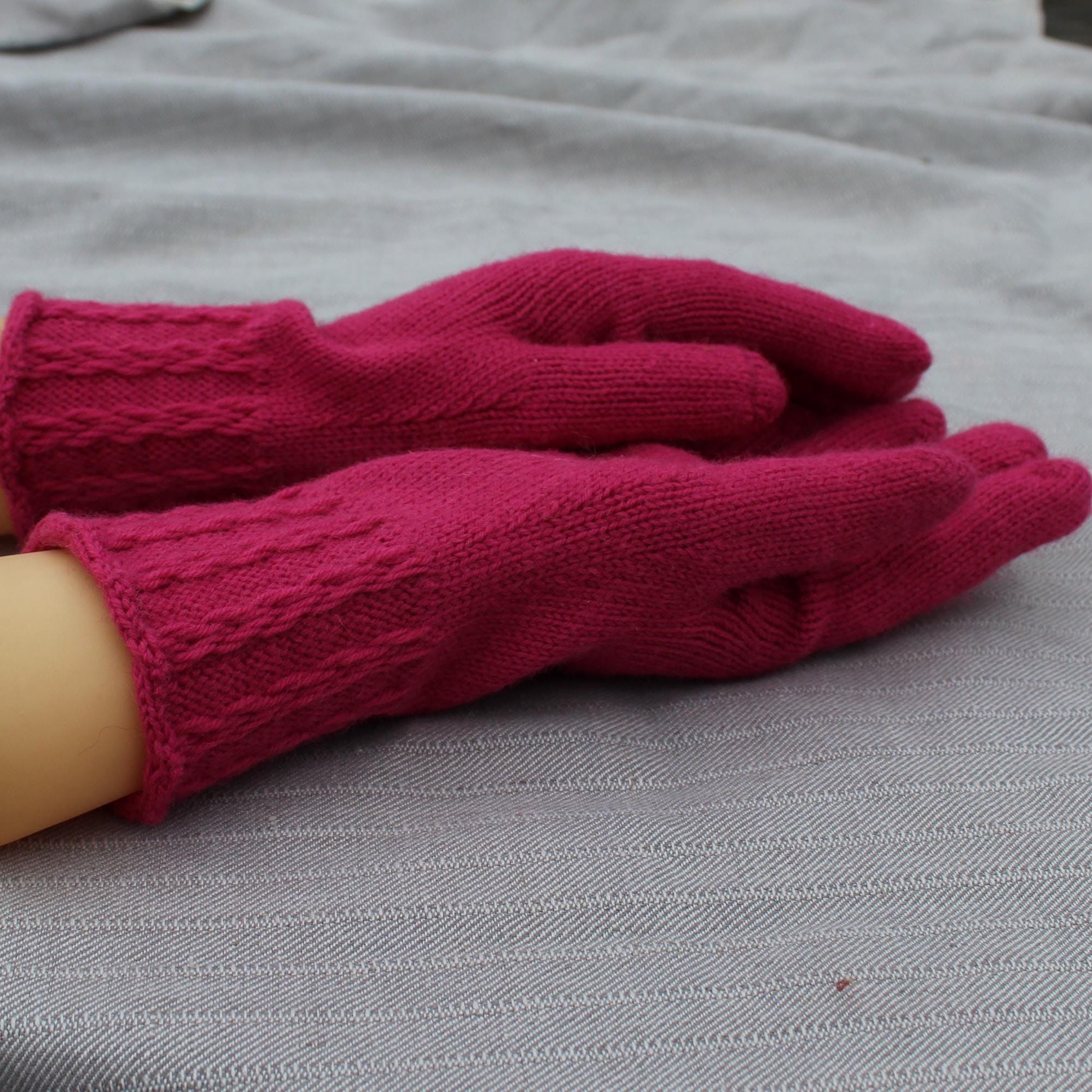 Pair of pink gloves on a mannequin hand against a gray fabric background