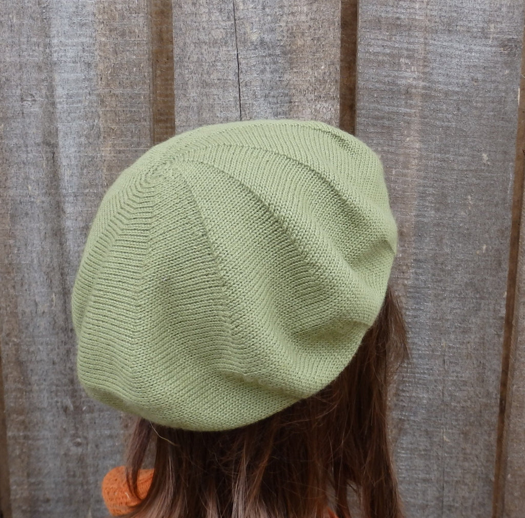Green knitted beret worn by a person against a wooden background