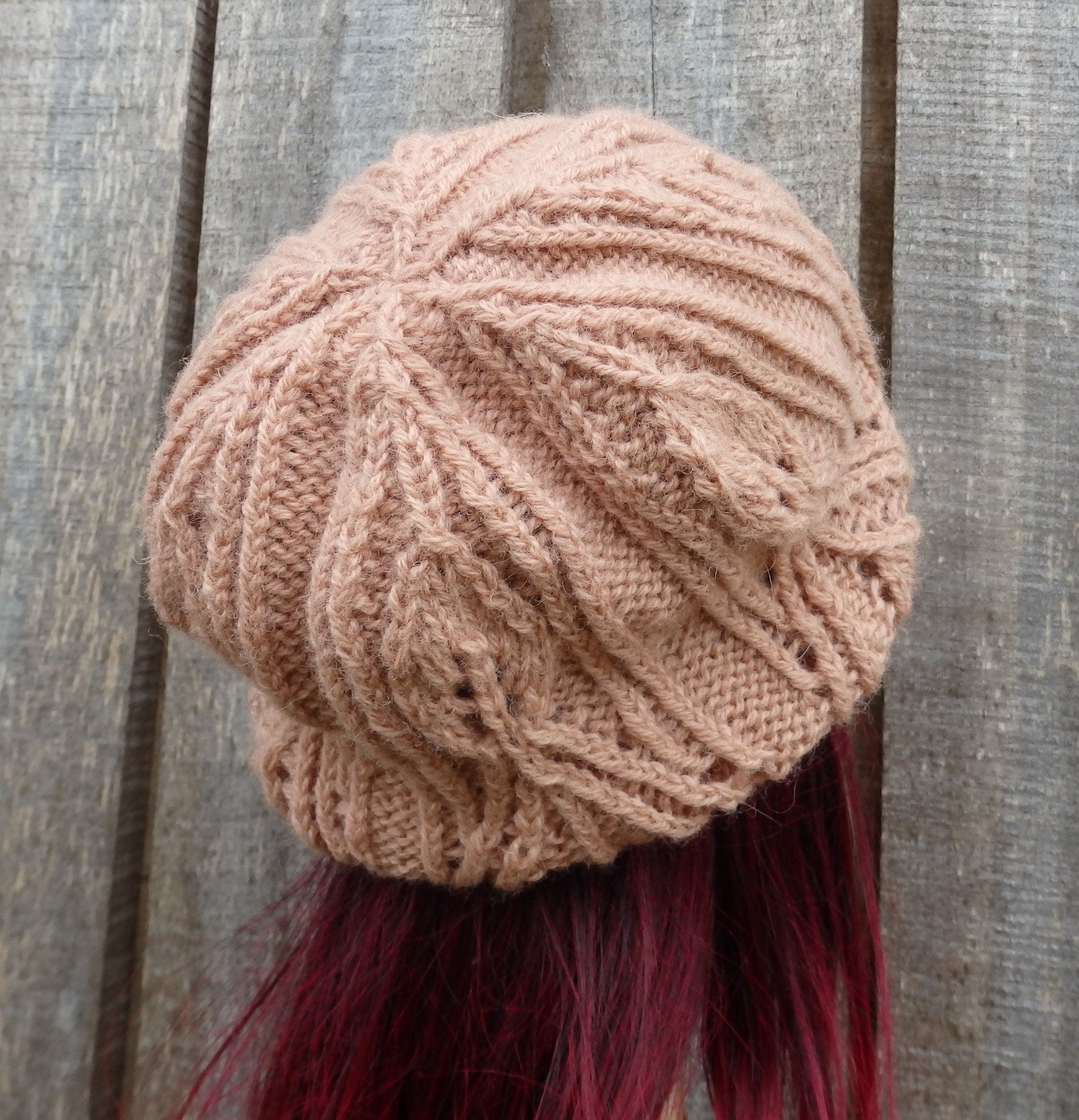 Knitted beige beanie on a person with red hair against a wooden background