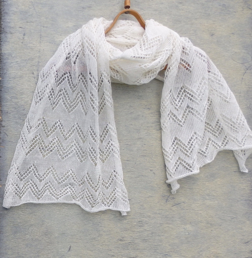 White lace shawl on a wooden hanger against a gray background