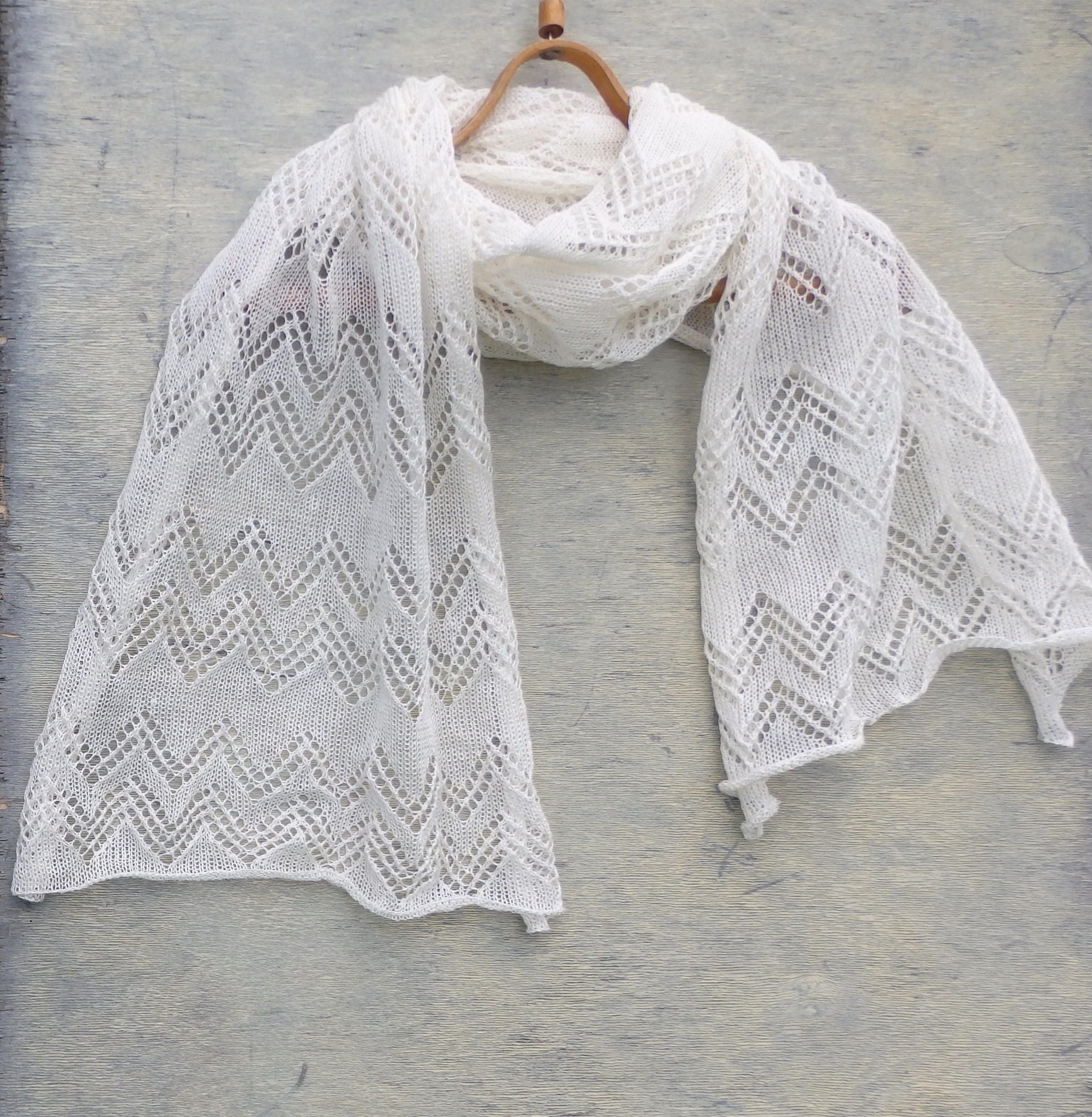 White lace shawl on a wooden hanger against a gray background