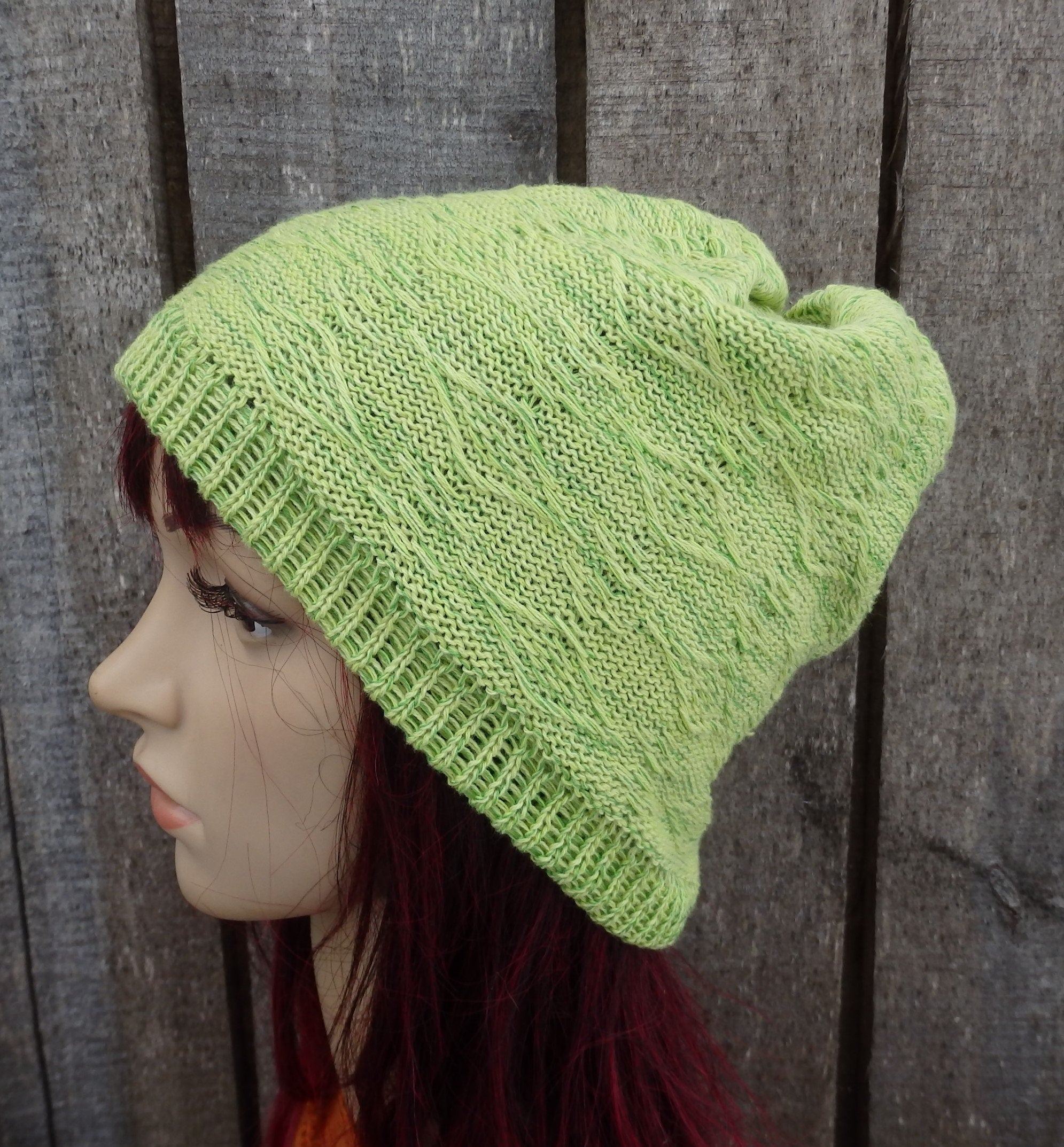Green knitted beanie on a mannequin head against a wooden background