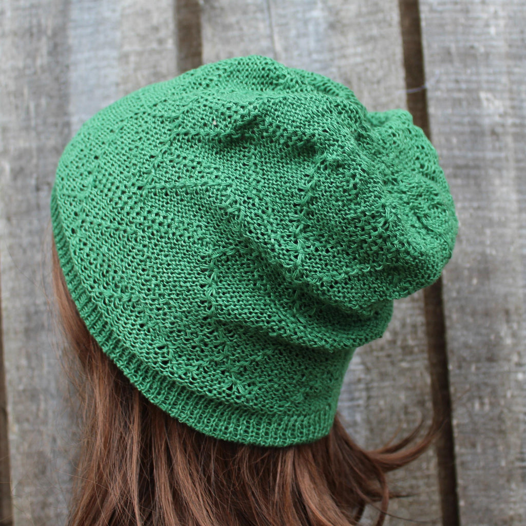 Green knitted beanie worn by a person with brown hair against a wooden background