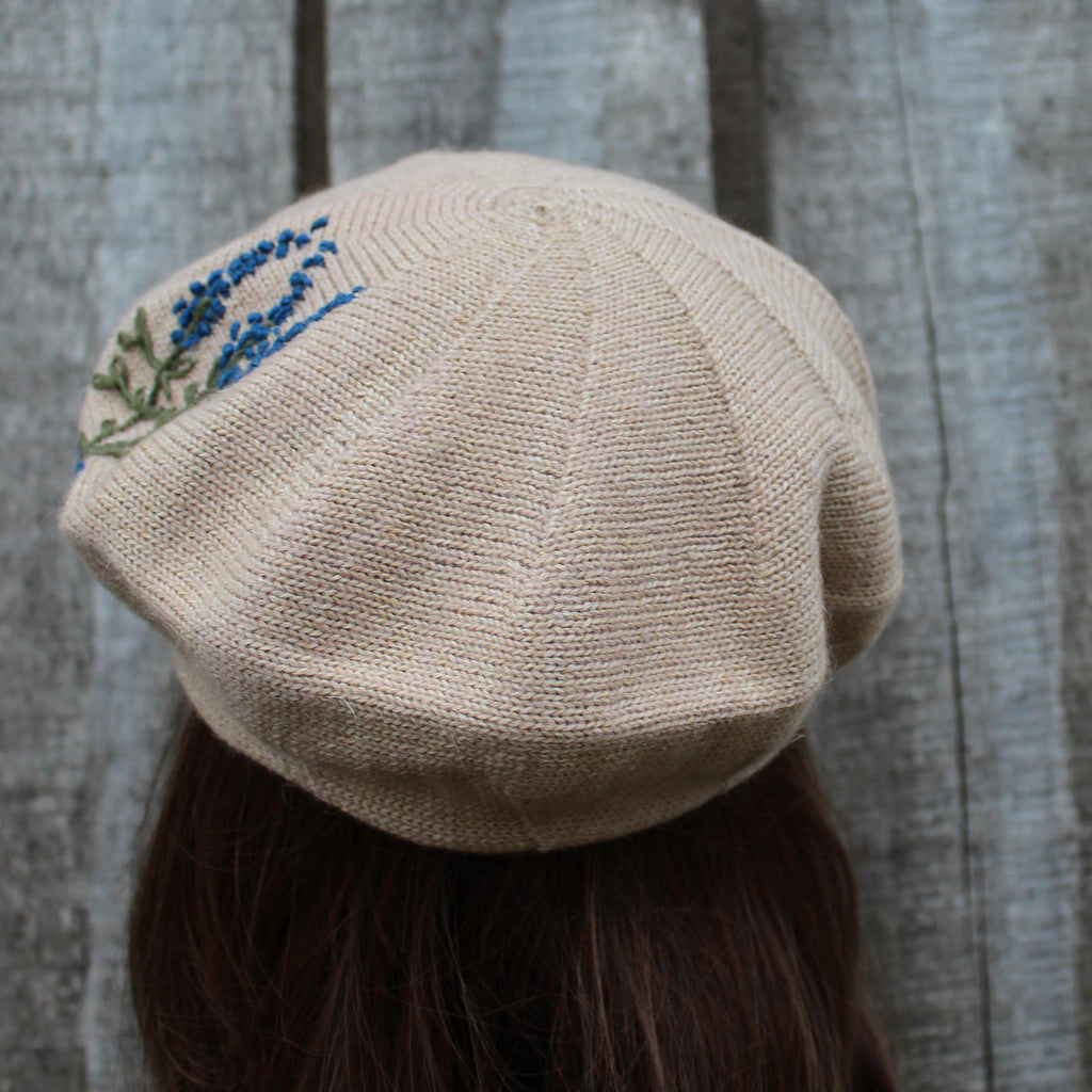 Beige knit cap with embroidered floral design on a textured gray background