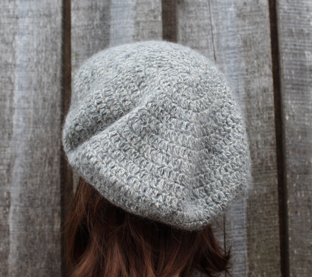Gray knitted beanie worn by a person against a wooden background