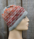 Knitted hat with gray, orange, and red pattern on a mannequin head against a wooden background