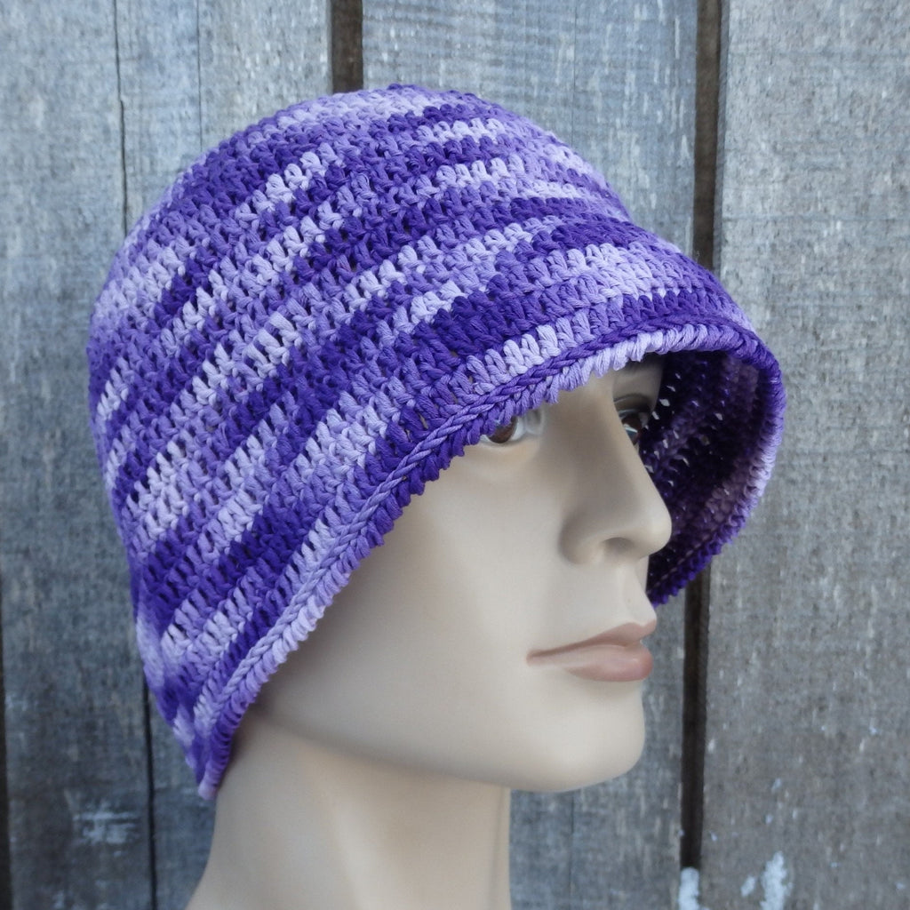 Colorful purple crocheted hat on a mannequin head against a textured gray background
