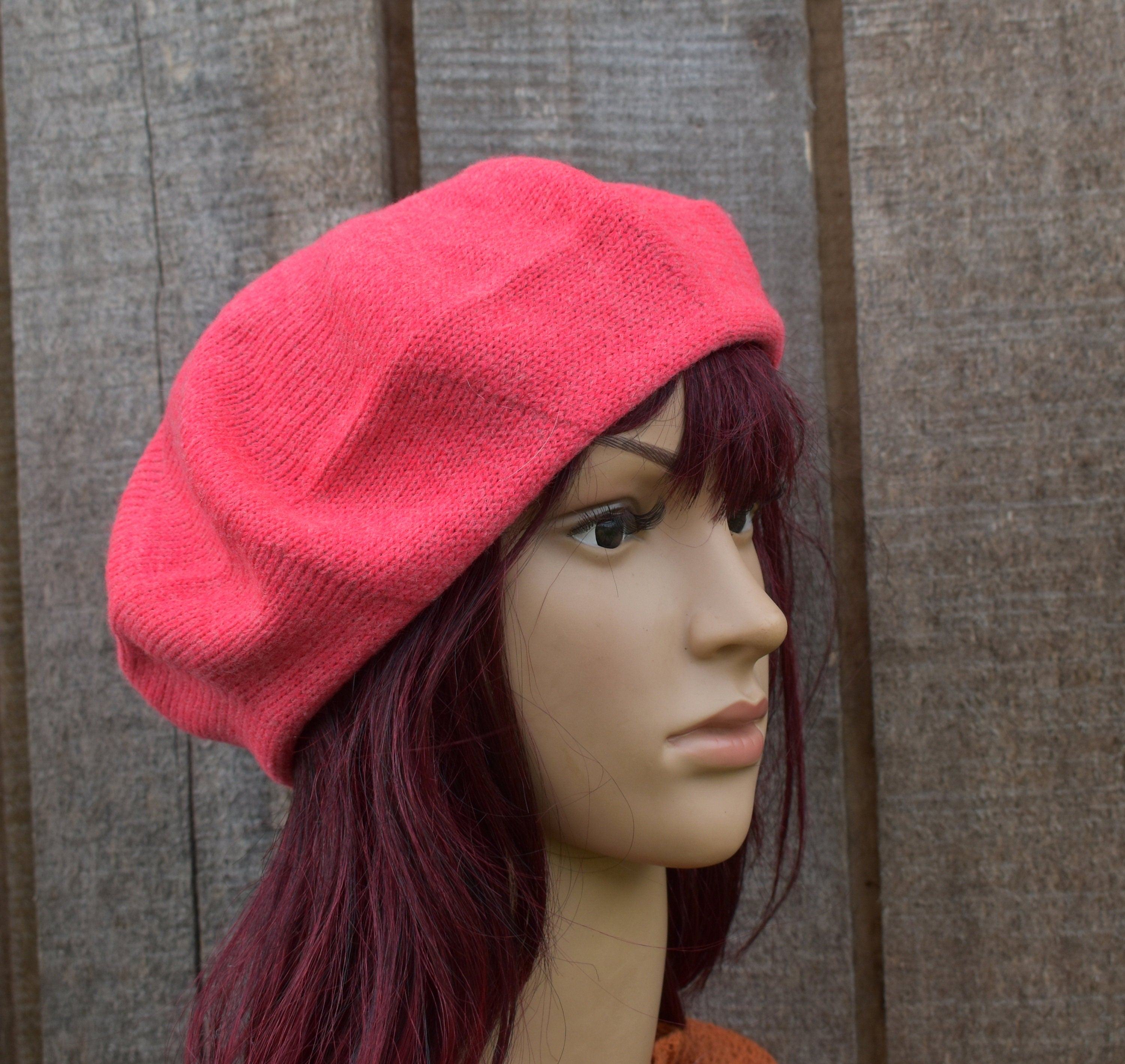 Mannequin head wearing a bright pink beret against a wooden background