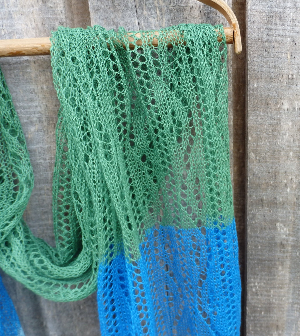 Green and blue knitted scarf on a wooden hanger against a wooden background