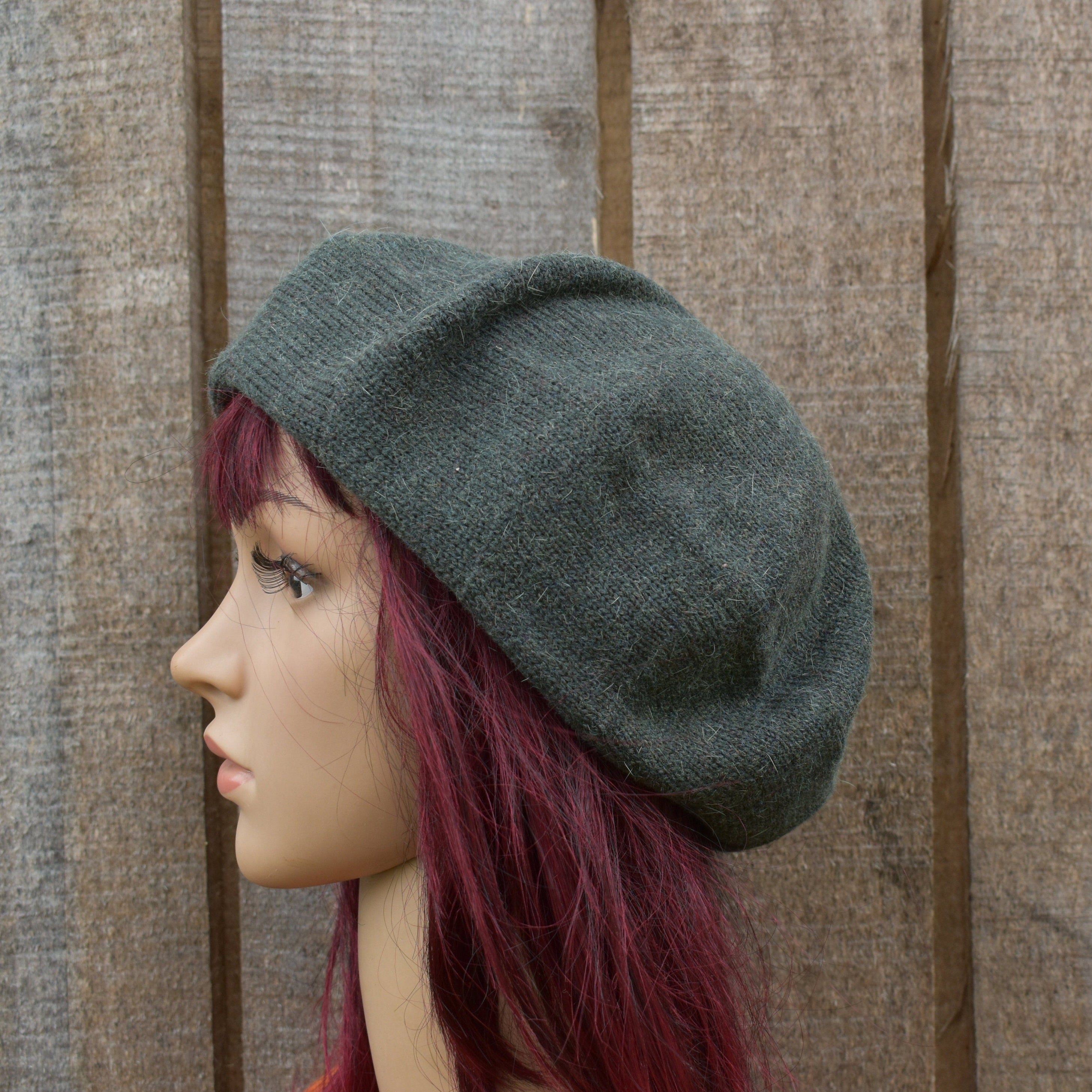 Mannequin head wearing a grey beret against a wooden background