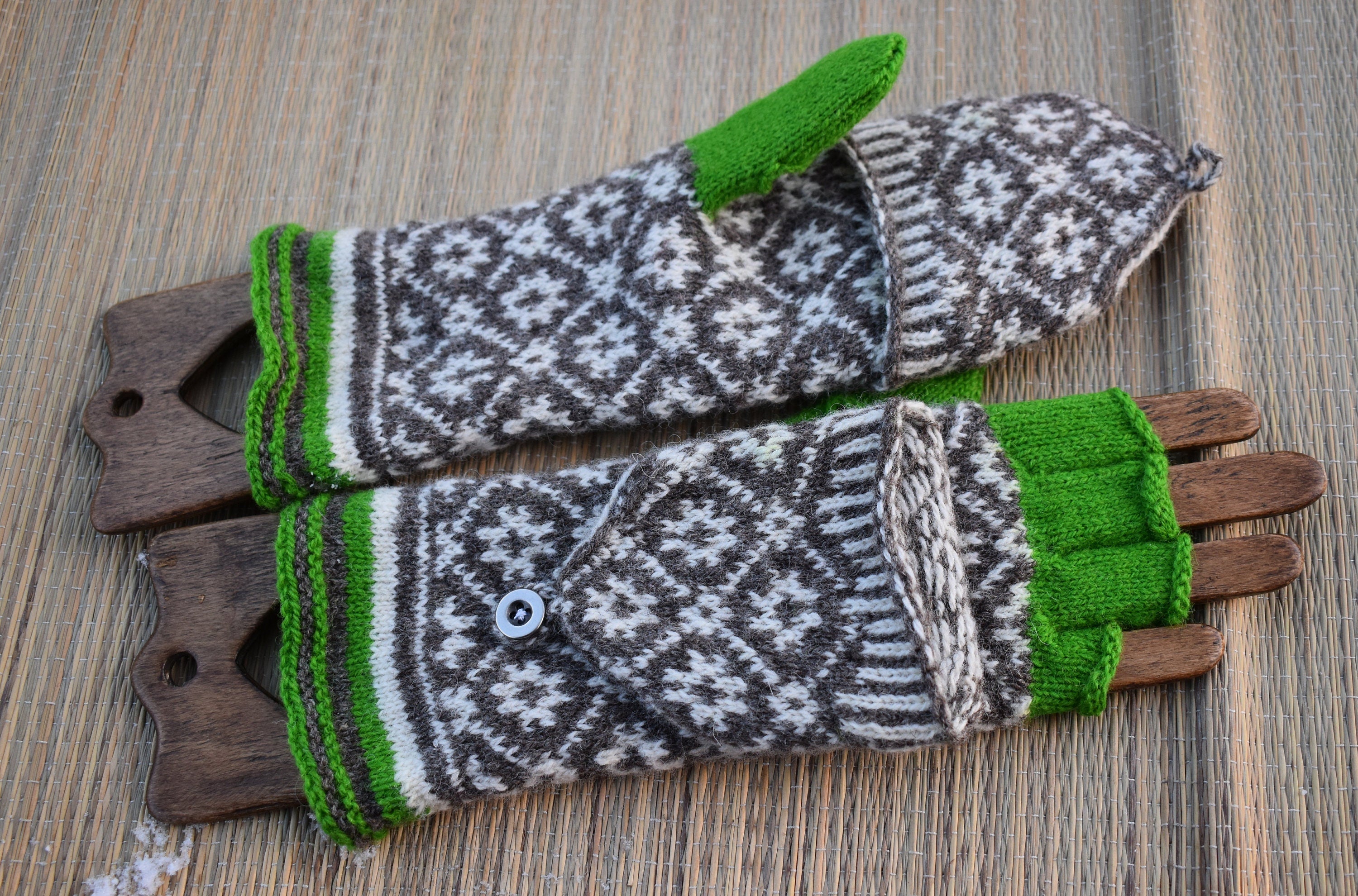 Pair of knitted mittens with green cuffs and tips on a wooden surface