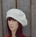 Mannequin head wearing a white knit beret against a wooden panel background