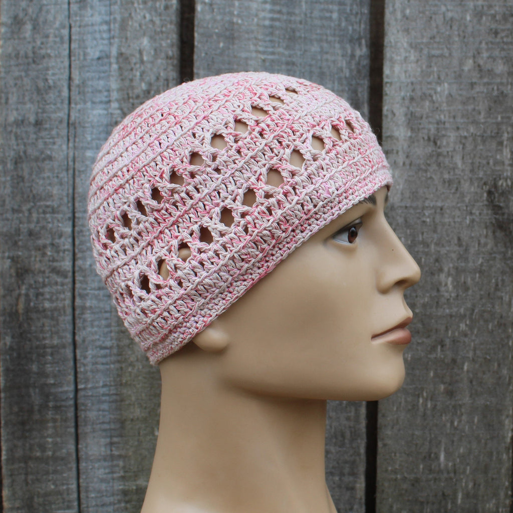 Pink crochet hat on a mannequin head against a wooden background