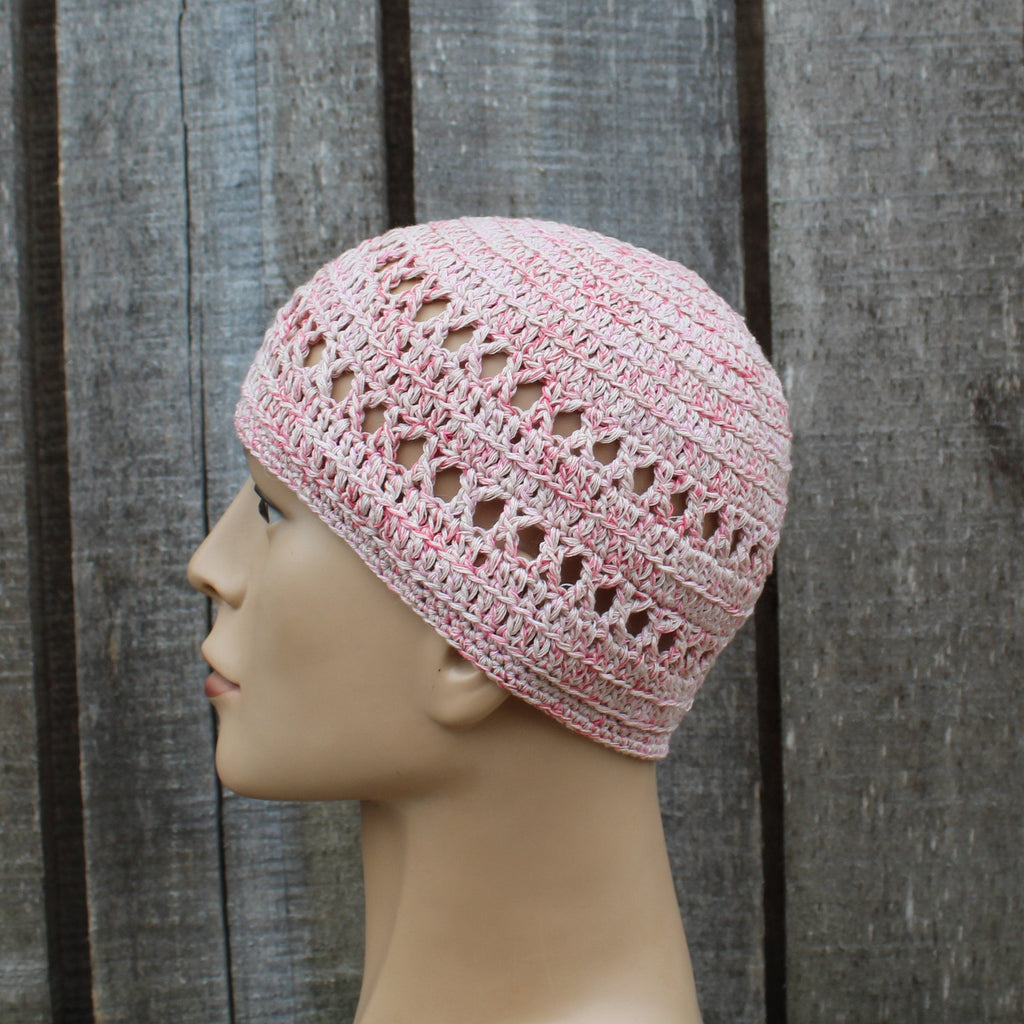 Pink crochet hat on a mannequin head against a wooden background