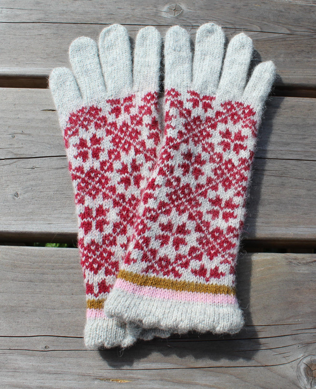 Pair of knitted gloves with a red and white pattern on a wooden surface