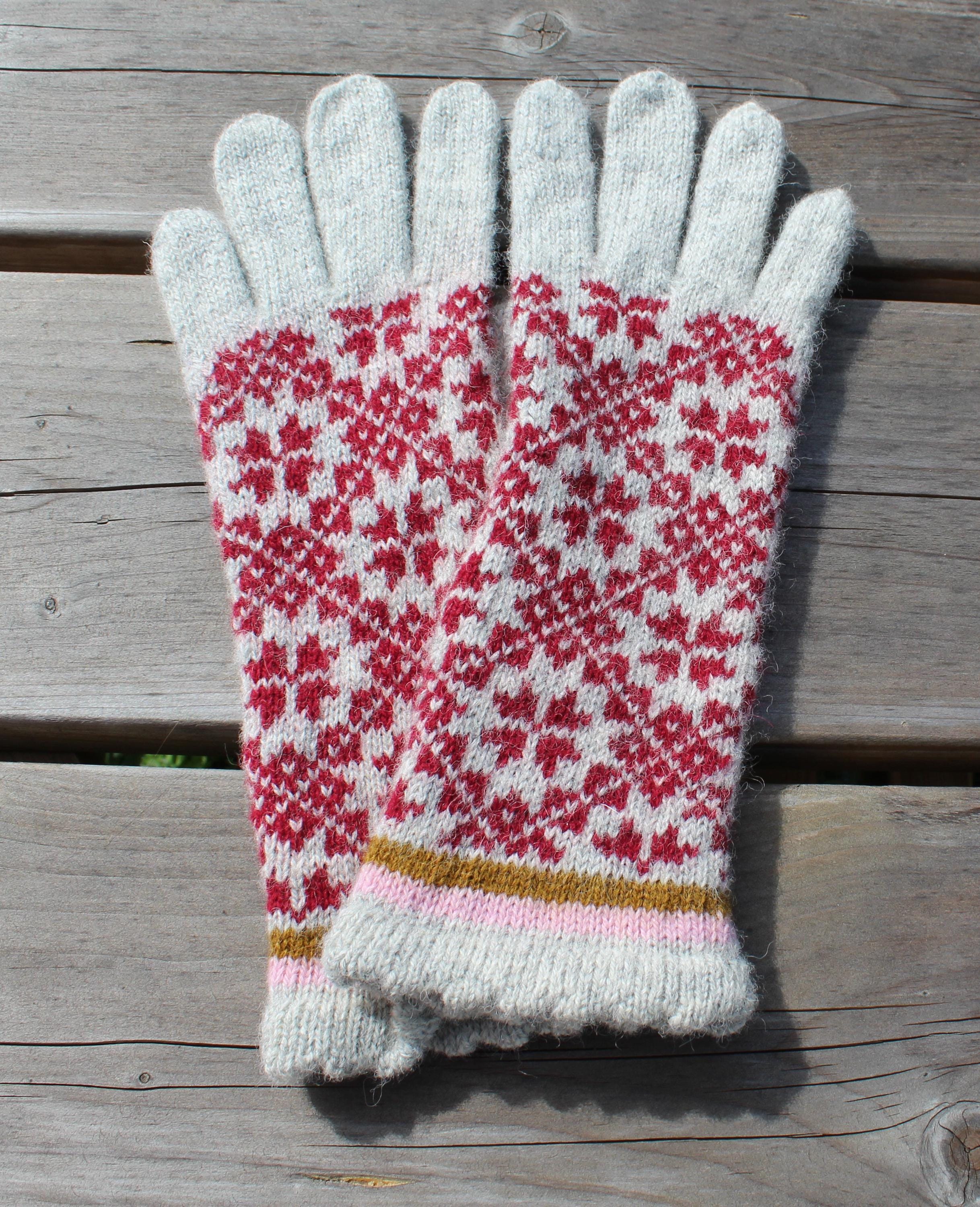 Pair of knitted gloves with a red and white pattern on a wooden surface