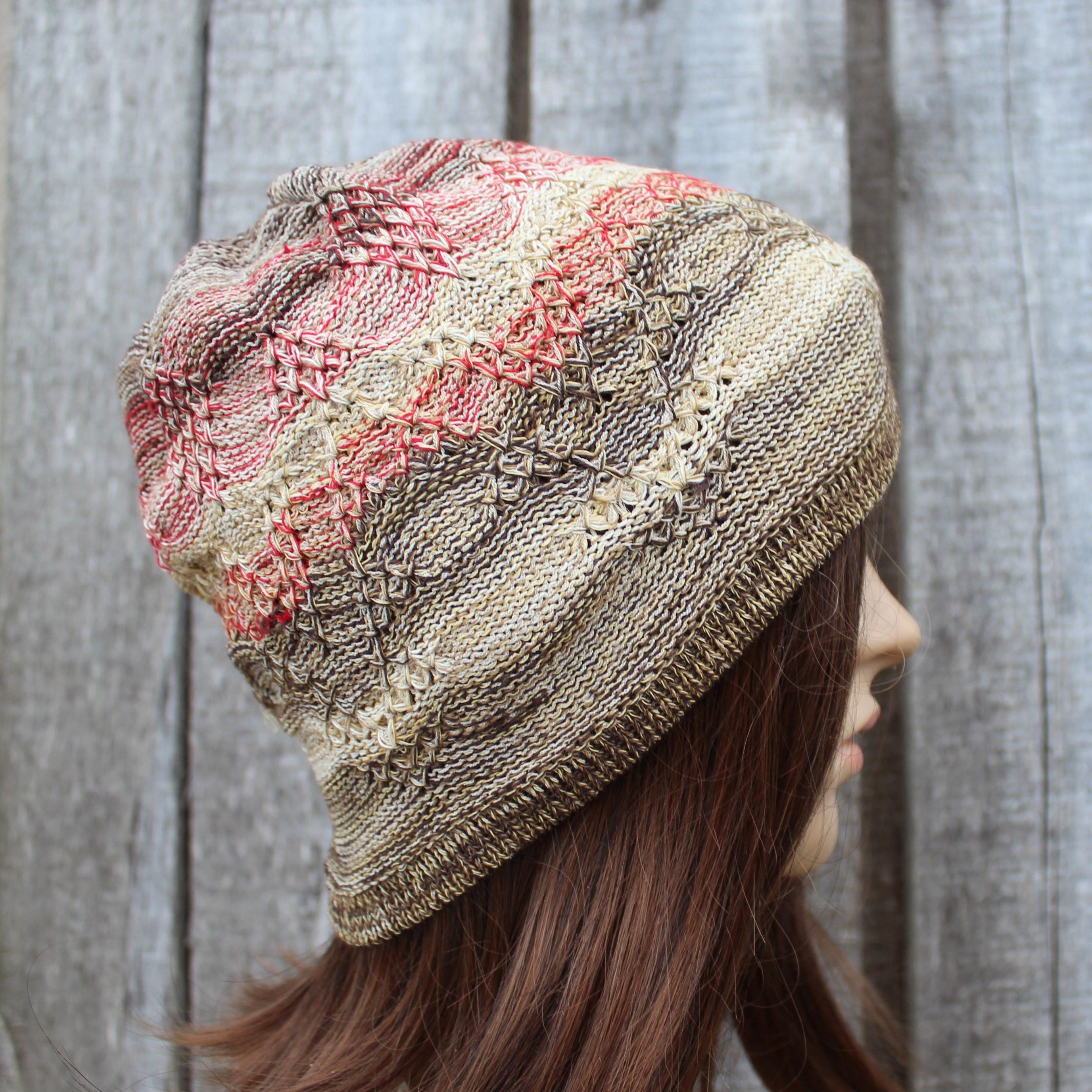 Knitted hat with pink and beige pattern worn by a person against a wooden fence background