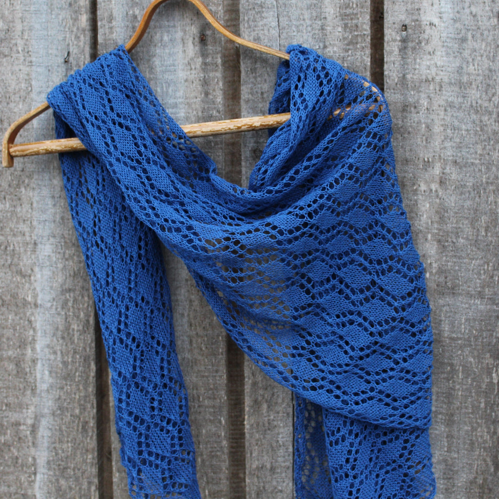 Blue knitted shawl on a wooden hanger against a wooden background