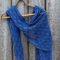 Blue knitted shawl on a wooden hanger against a wooden background