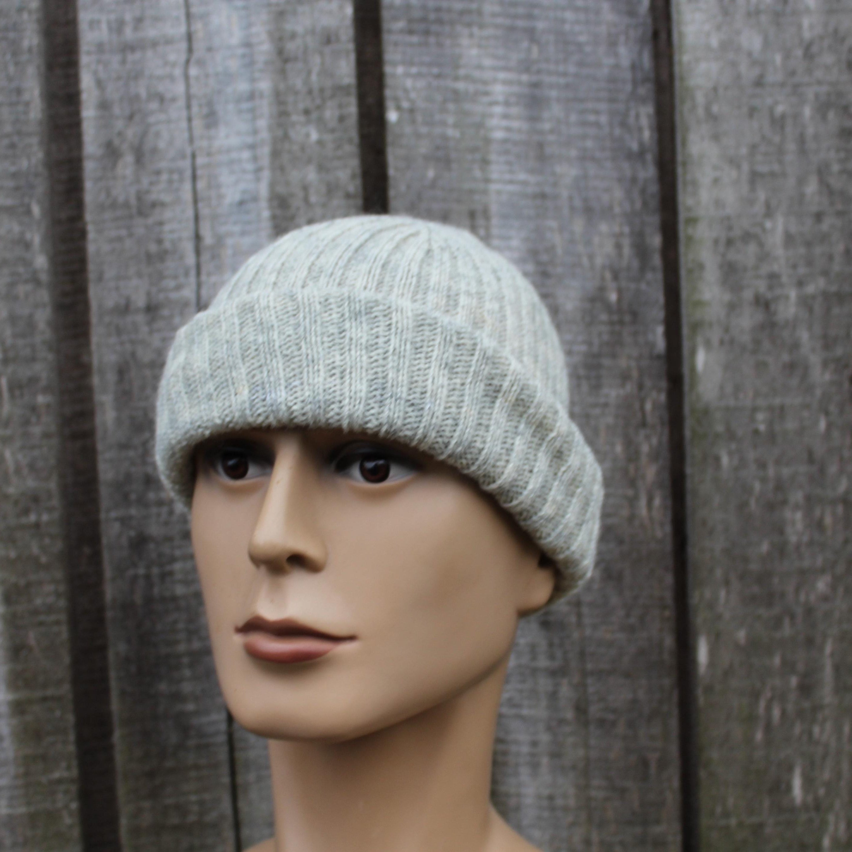 Mannequin head wearing a light gray knit beanie against a wooden panel background