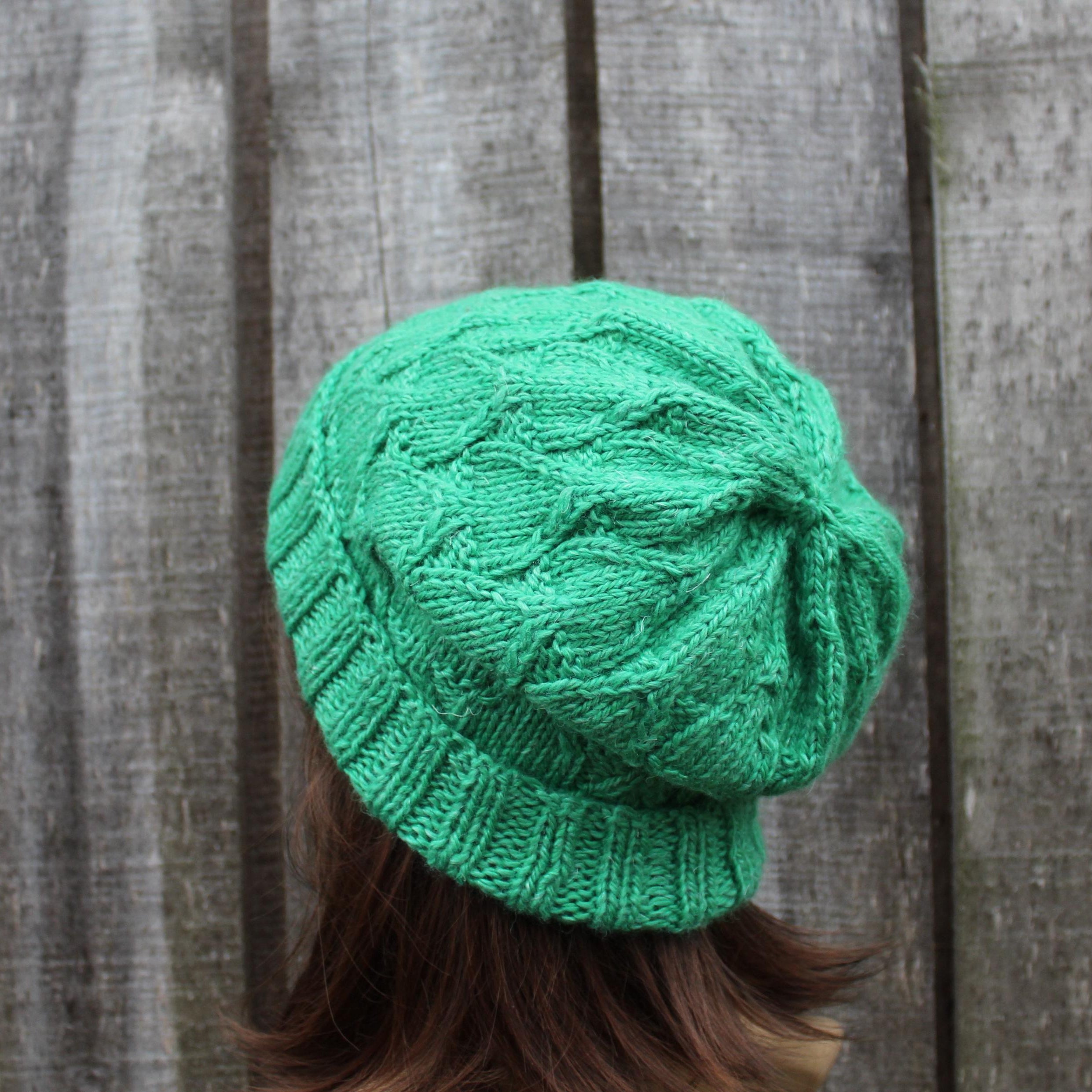 Green knitted beanie worn by a person against a wooden fence background