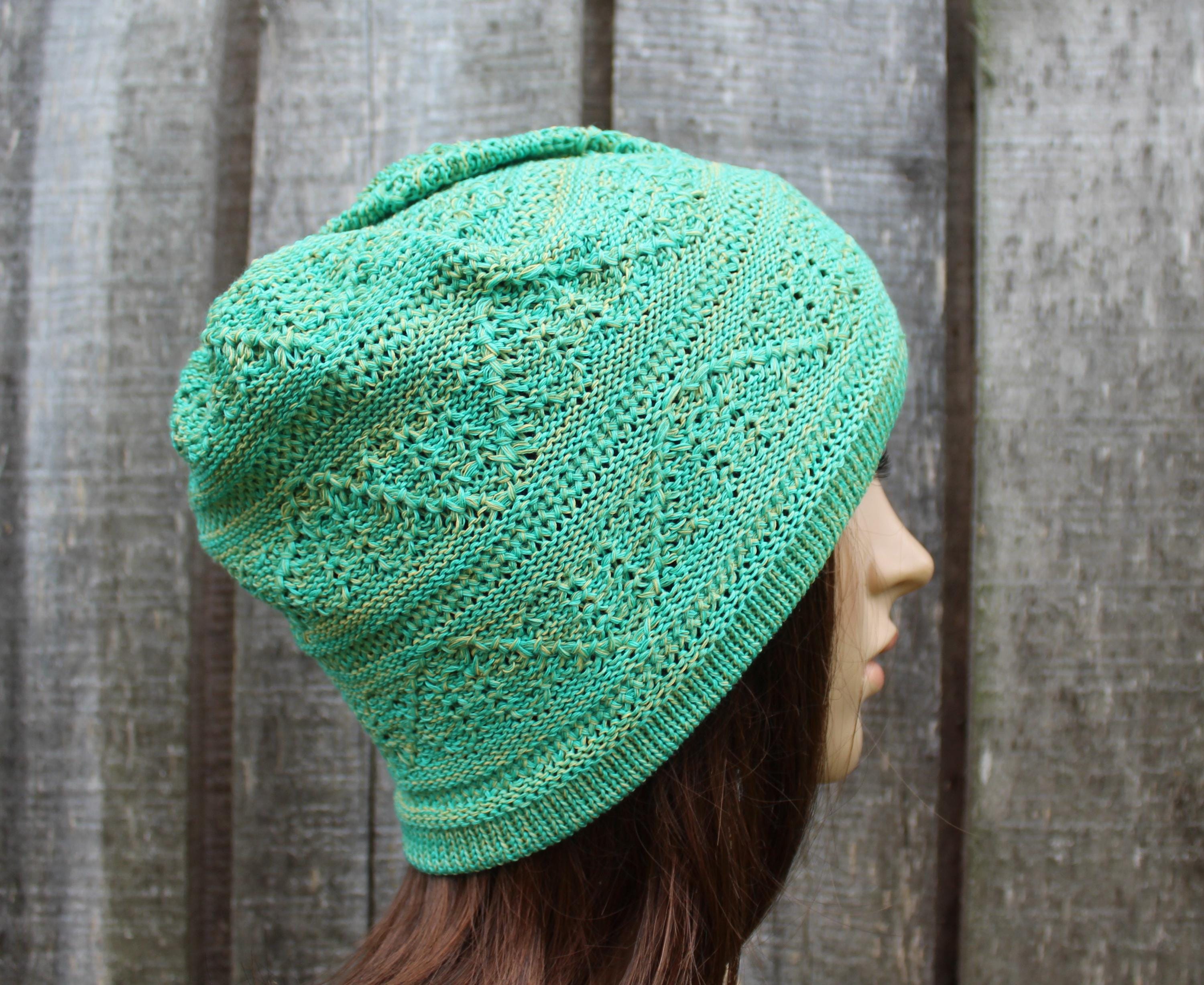 Green knitted hat worn by a person against a wooden fence background