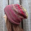 Knitted hat with a pink and green pattern worn by a person against a wooden background