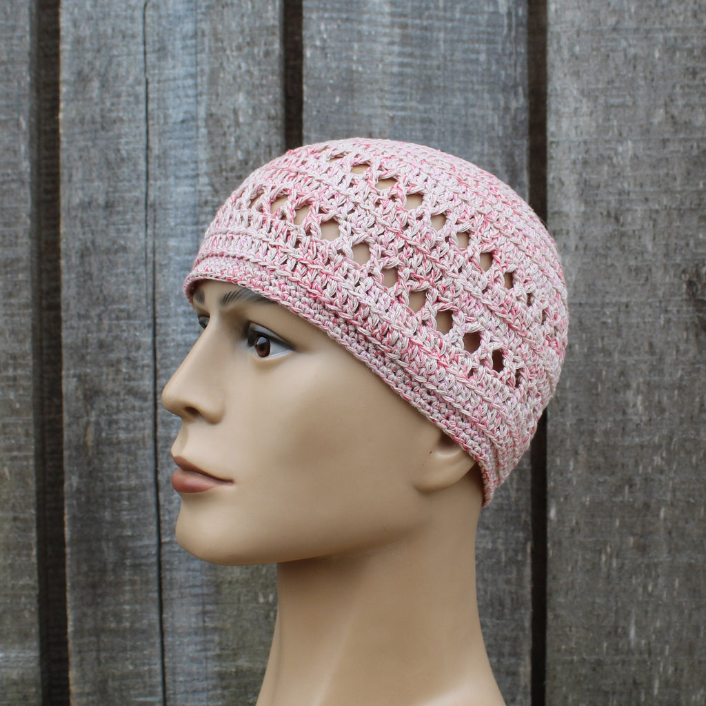 Pink crochet hat on a mannequin head against a wooden background