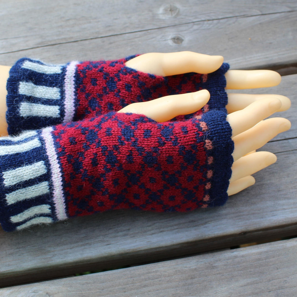 Pair of red and blue patterned fingerless gloves on a mannequin hand against a wooden background