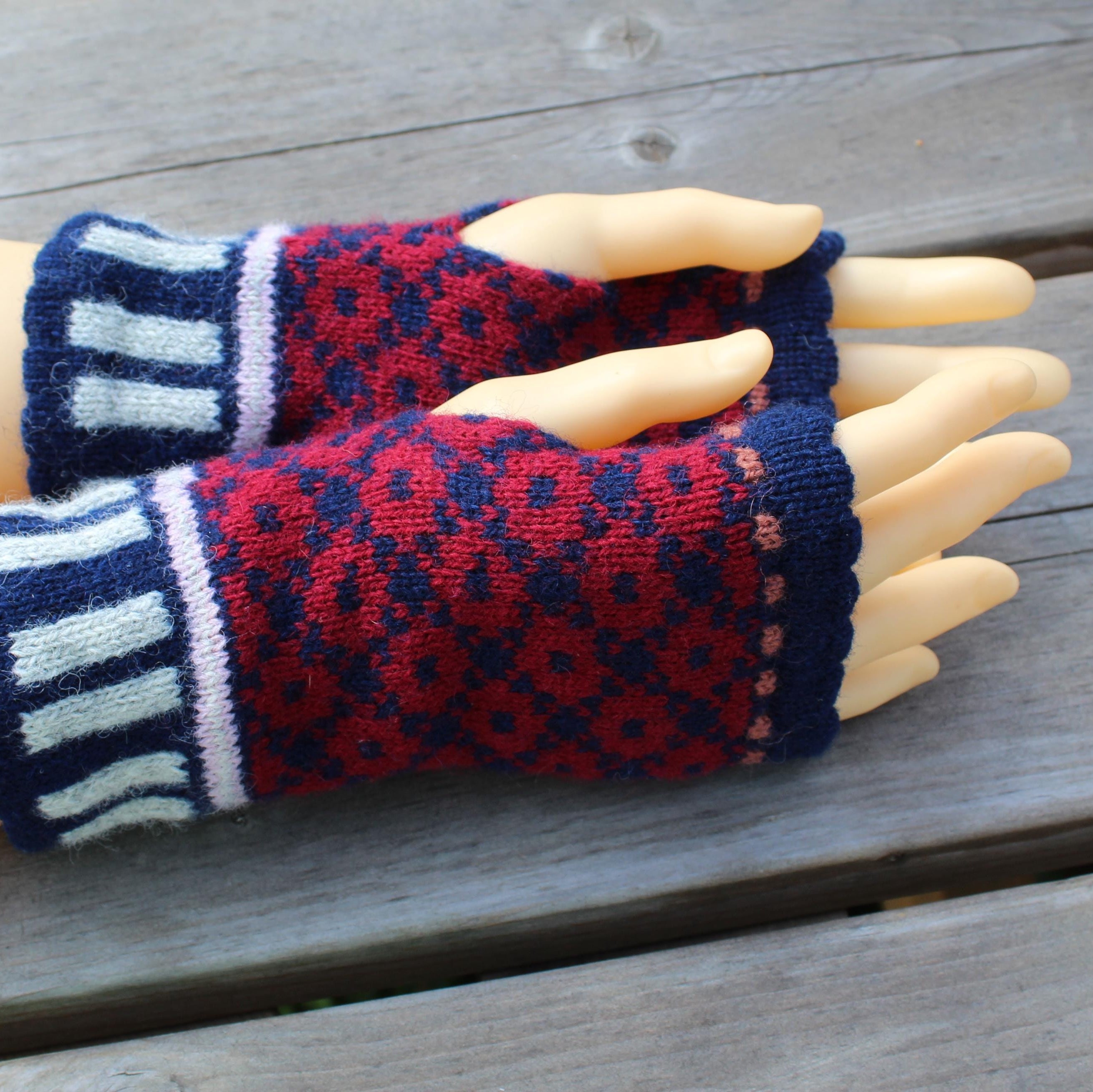 Pair of red and blue patterned fingerless gloves on a mannequin hand against a wooden background